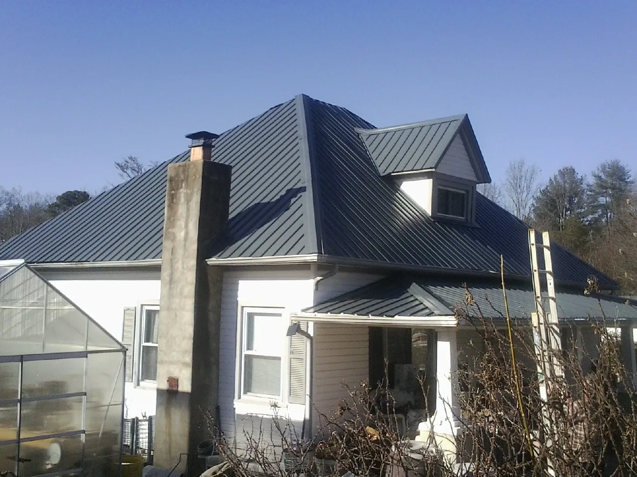 Dark blue standing seam metal roof on a white farmhouse with dormer — Slate & Tile Roof Repair by Roofing Brothers in Carpenter