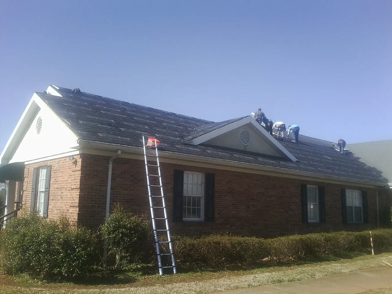 Crew tearing shingles off a brick ranch roof with a ladder set — Metal Roof Repair work by our crew in Carpenter
