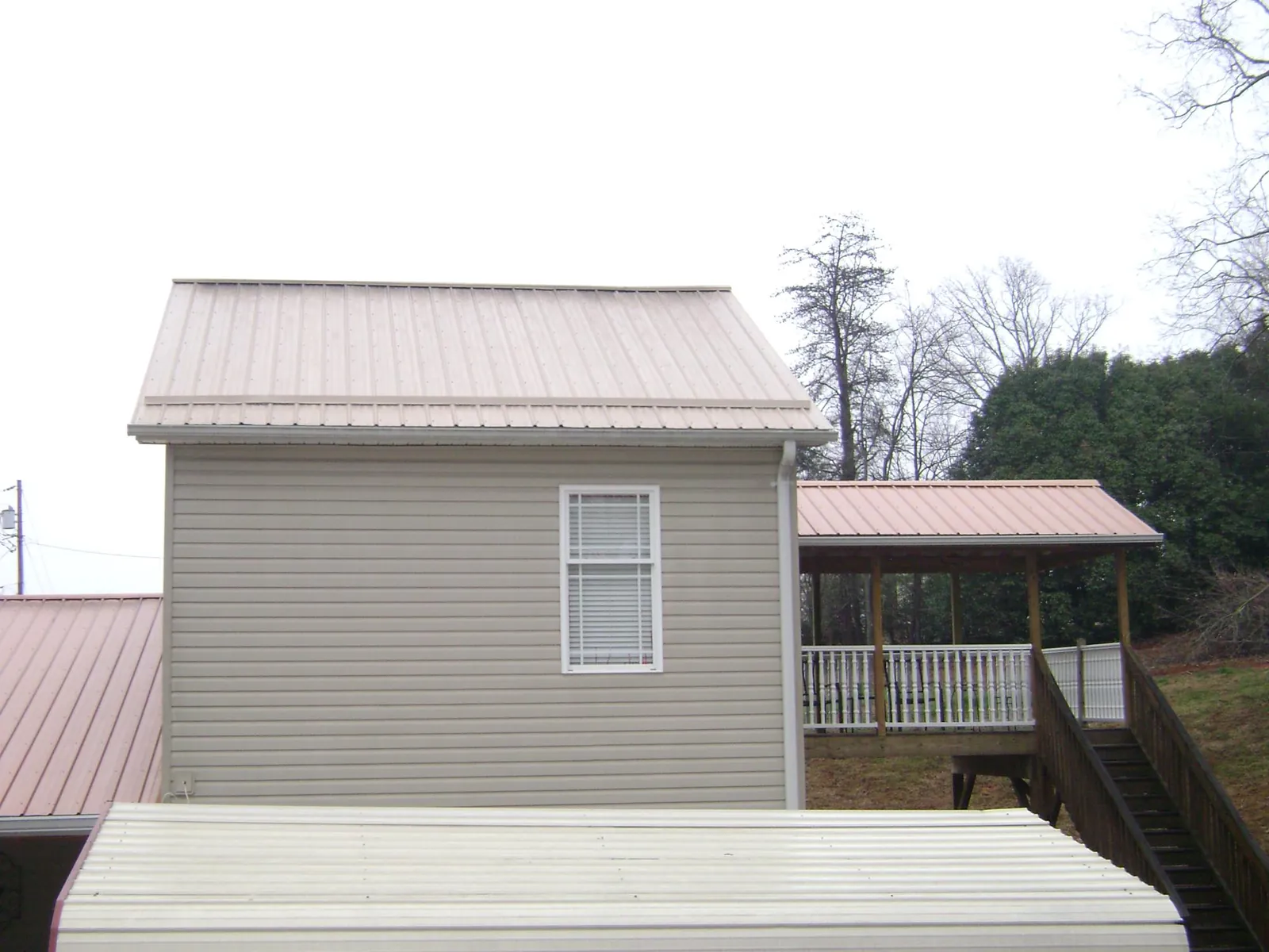 Tan metal roofs on a two story addition and attached porch, from a Roof Replacement job in Carpenter